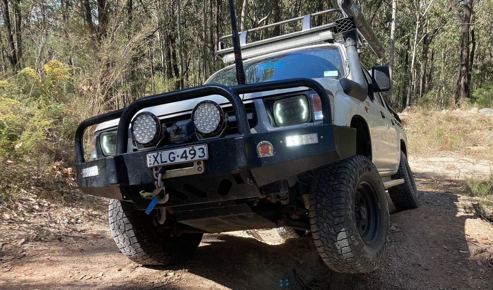 A rugged off-road vehicle equipped with spotlights and a sturdy front bumper, navigating through rough terrain in a natural setting.